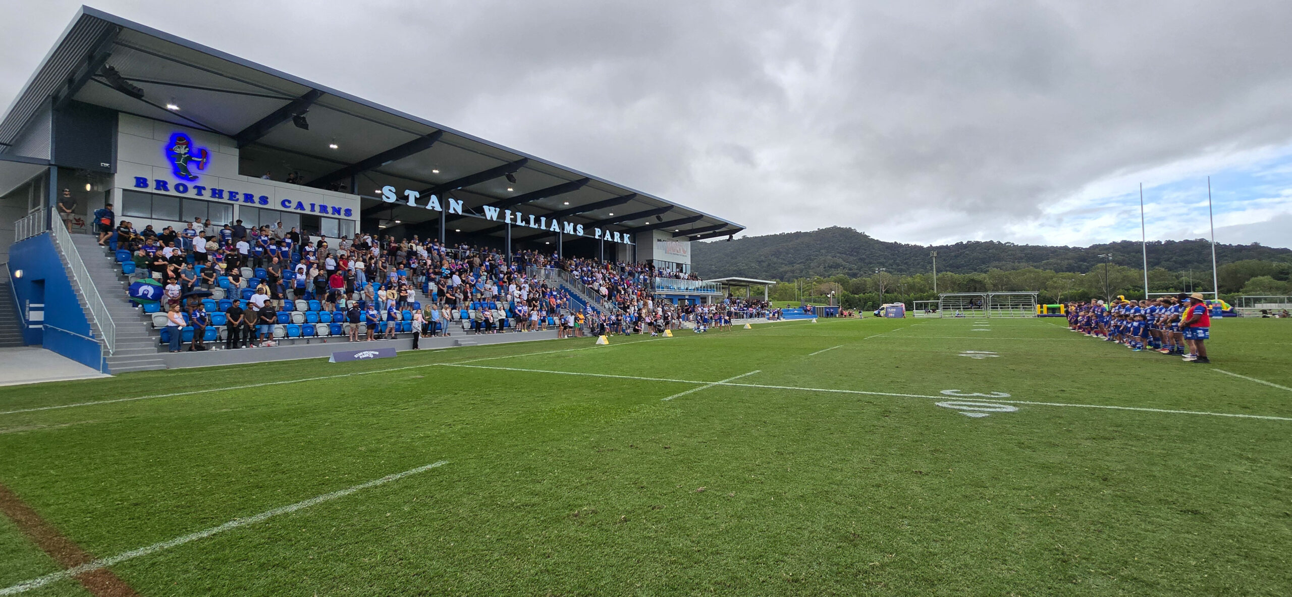 Football field with players and goal posts under cloudy sky.