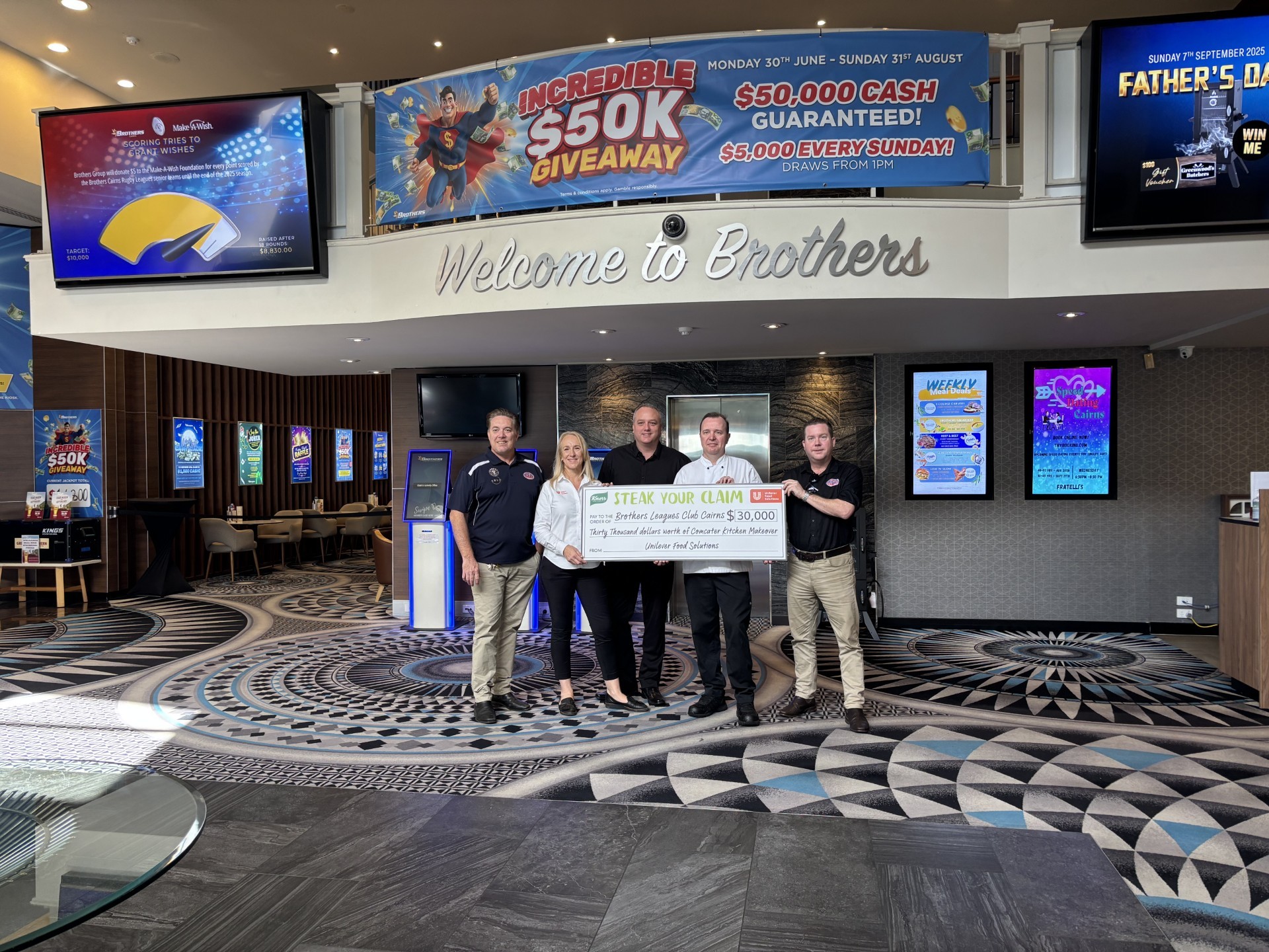 People standing near club entrance holding large cheque